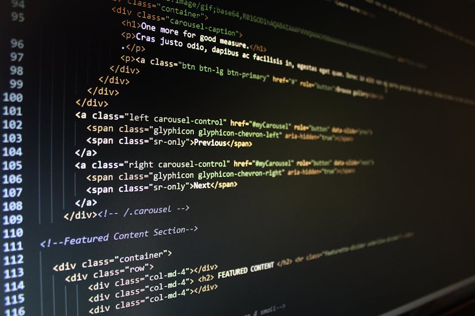 A person's hands are shown typing on a laptop keyboard placed on a dark surface. The laptop screen displays lines of code with colorful syntax highlighting, predominantly in dark mode. The background 